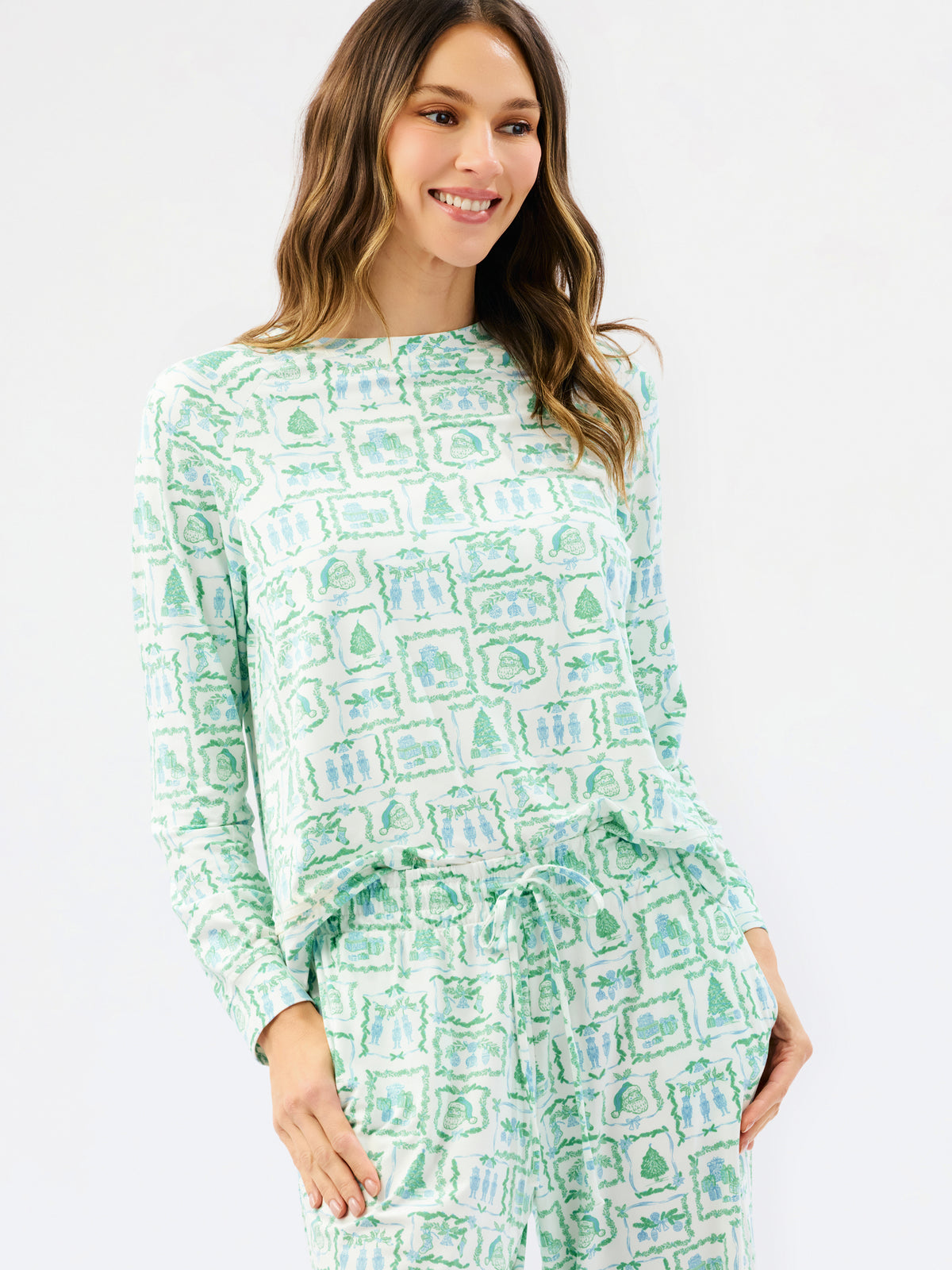 A woman modeling a matching two-piece lounge set featuring a light green and white watercolor-style pattern of houses and trees, with a long-sleeve top and drawstring waist.