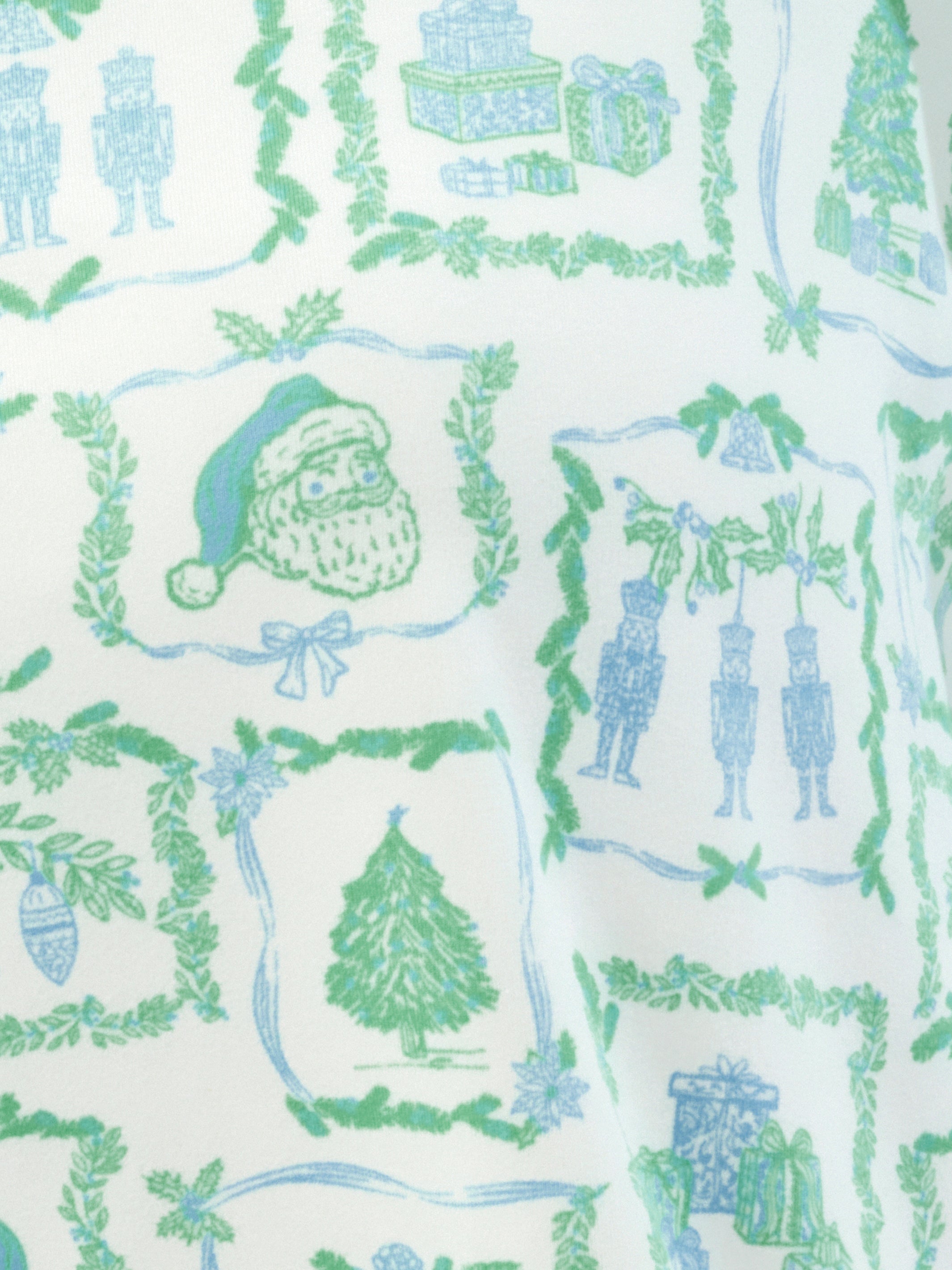 A close-up of a holiday-themed fabric pattern featuring green wreaths, garlands, nutcricks, presents, and a Santa hat on an off-white background.