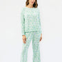 A woman modeling a two-piece pajama set with a light green and white abstract pattern, consisting of a long-sleeve top and matching pants, against a plain white studio background.