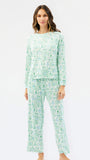 A woman modeling a two-piece long-sleeve pajama set with a light mint green and white pattern of small illustrated icons, shot against a plain white studio background.