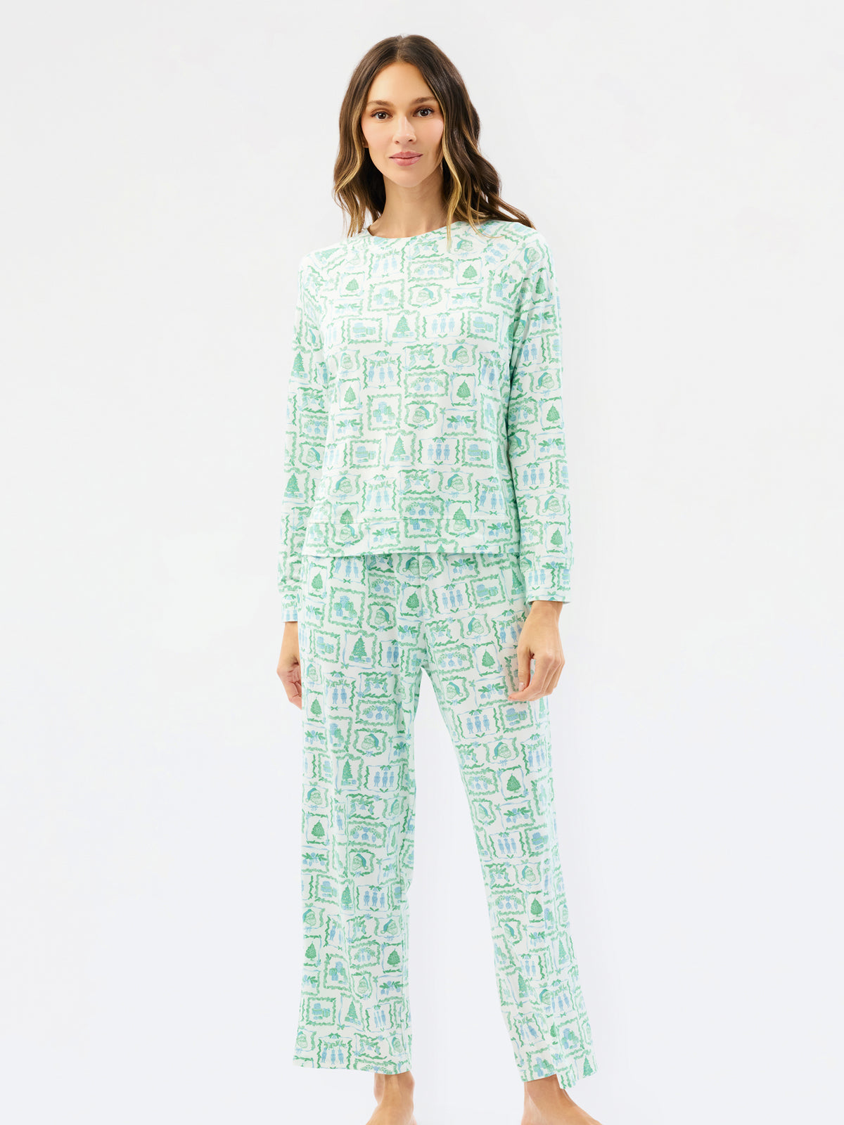 A woman modeling a two-piece long-sleeve pajama set with a light mint green and white pattern of small illustrated icons, shot against a plain white studio background.