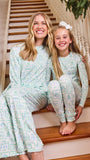 A woman and a young girl sitting together on wooden stairs indoors, wearing matching long-sleeve pajamas with a pale mint green and white ornamental pattern.