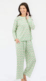 A woman modeling a two-piece pajama set with a light green and white pattern of small illustrated figures, photographed against a plain white studio background.
