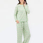 A woman modeling a two-piece pajama set with a light green and white pattern of small illustrated figures, photographed against a plain white studio background.