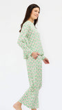 A woman modeling a two-piece long-sleeve pajama set with a green and pink pine tree pattern, shown from a side profile against a plain white background.