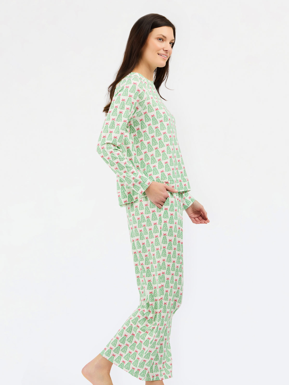 A woman modeling a two-piece long-sleeve pajama set with a green and pink pine tree pattern, shown from a side profile against a plain white background.
