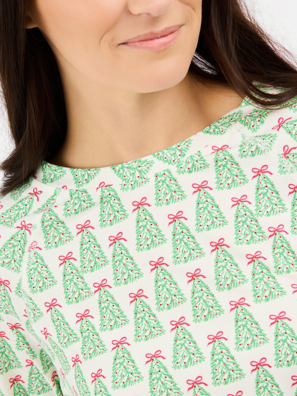A close-up of a woman wearing a cream-colored top with a repeating pattern of green Christmas trees tied with red bows.