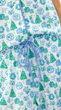 A close-up of a sleeveless white top or dress with an allover Christmas-themed print in blue and green, featuring a blue drawstring at the waist. The print includes gift boxes, Christmas trees, ornaments, and snowflakes.