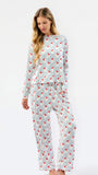 A woman modeling a matching long-sleeve pajama set with a white base, thin vertical blue stripes, and a scattered red abstract pattern, photographed against a plain white studio background.