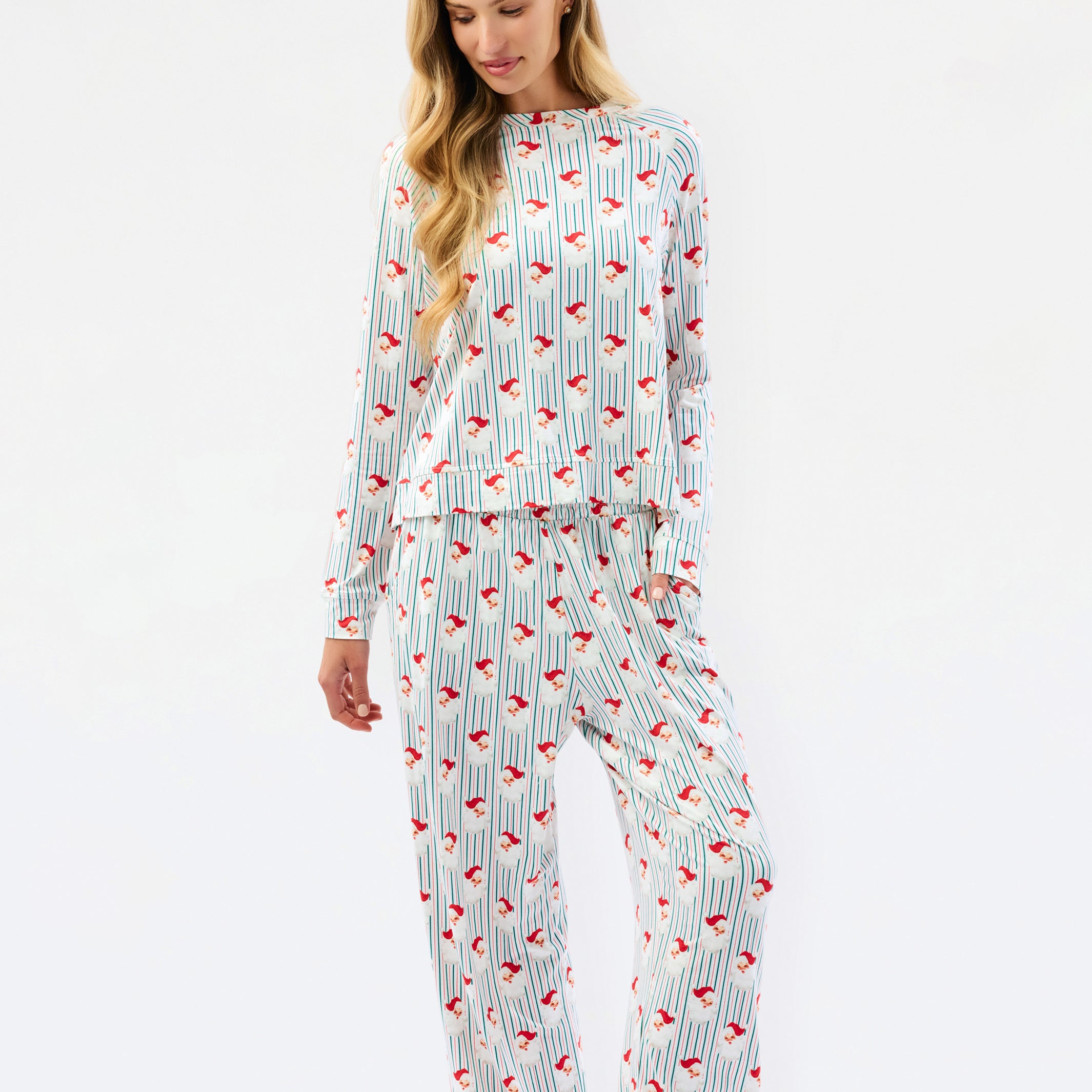 A woman modeling a matching long-sleeve pajama set with a white base, thin vertical blue stripes, and a scattered red abstract pattern, photographed against a plain white studio background.