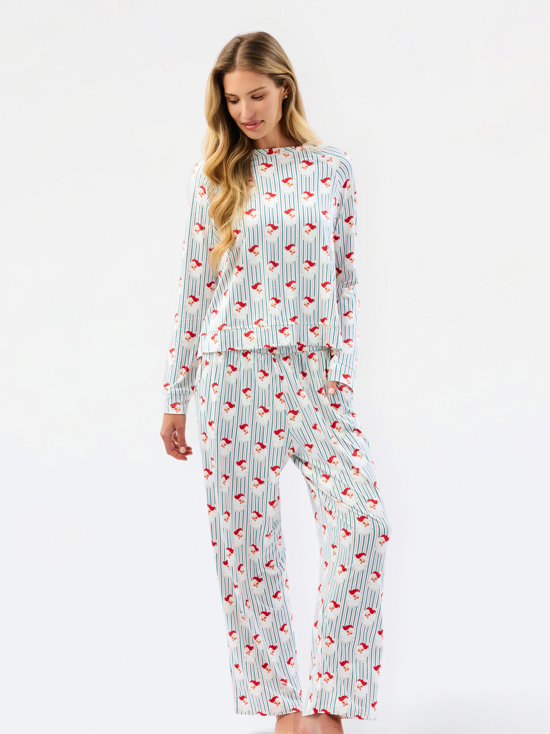 A woman modeling a matching long-sleeve pajama set with a white base, thin vertical blue stripes, and a scattered red abstract pattern, photographed against a plain white studio background.