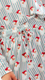 A close-up of a holiday-themed pajama set featuring a festive print of Santa Claus faces over vertical red, green, and white stripes, with a matching drawstring waist.