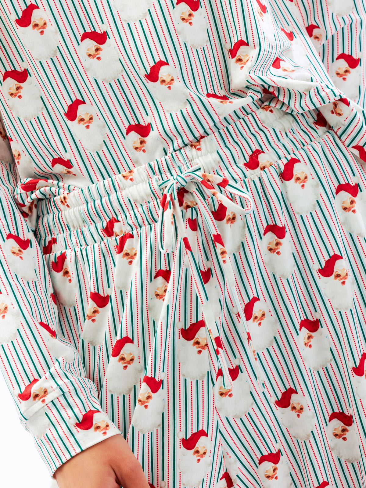 A close-up of a holiday-themed pajama set featuring a festive print of Santa Claus faces over vertical red, green, and white stripes, with a matching drawstring waist.