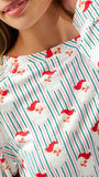A close-up of a person wearing a white long-sleeve top with a festive Christmas print featuring green and red vertical stripes and Santa Claus faces.