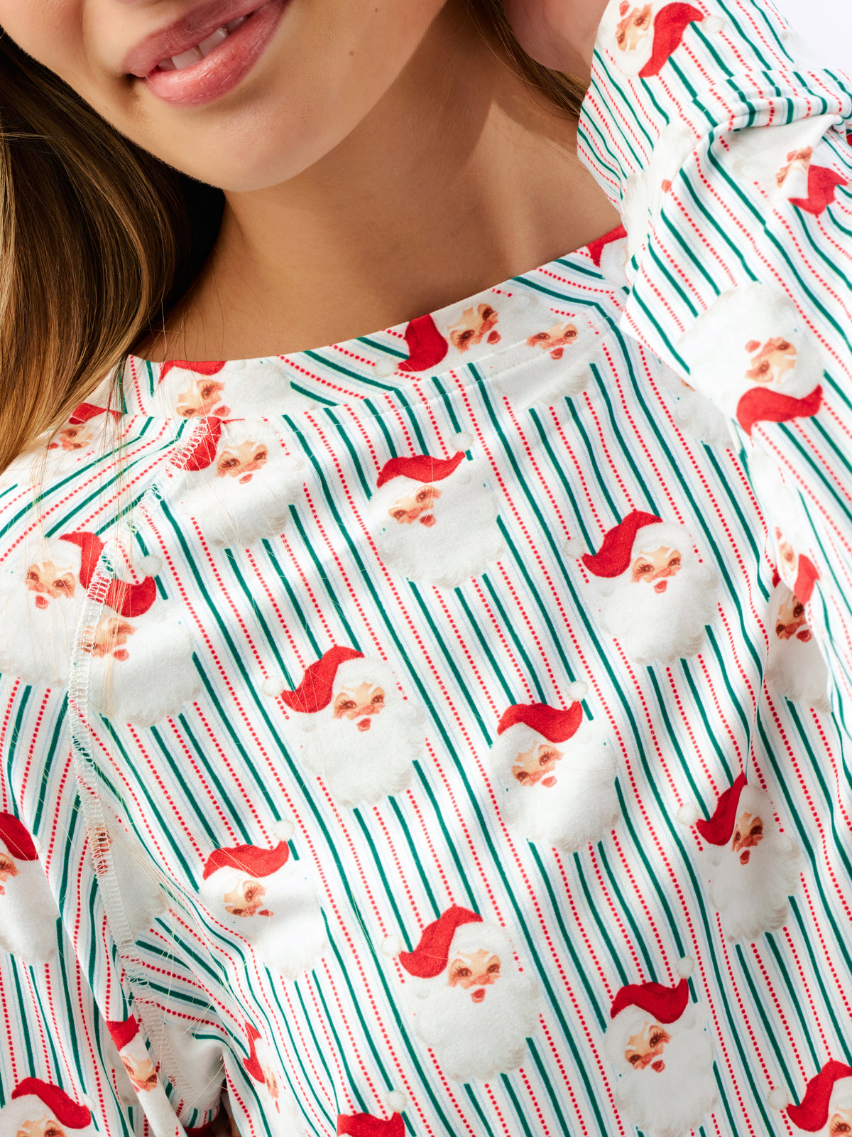 A close-up of a person wearing a white long-sleeve top with a festive Christmas print featuring green and red vertical stripes and Santa Claus faces.
