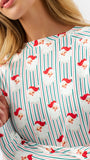 A close-up of a woman wearing a long-sleeve top with a festive holiday print of Santa Claus faces over a white background with thin red and green vertical stripes.