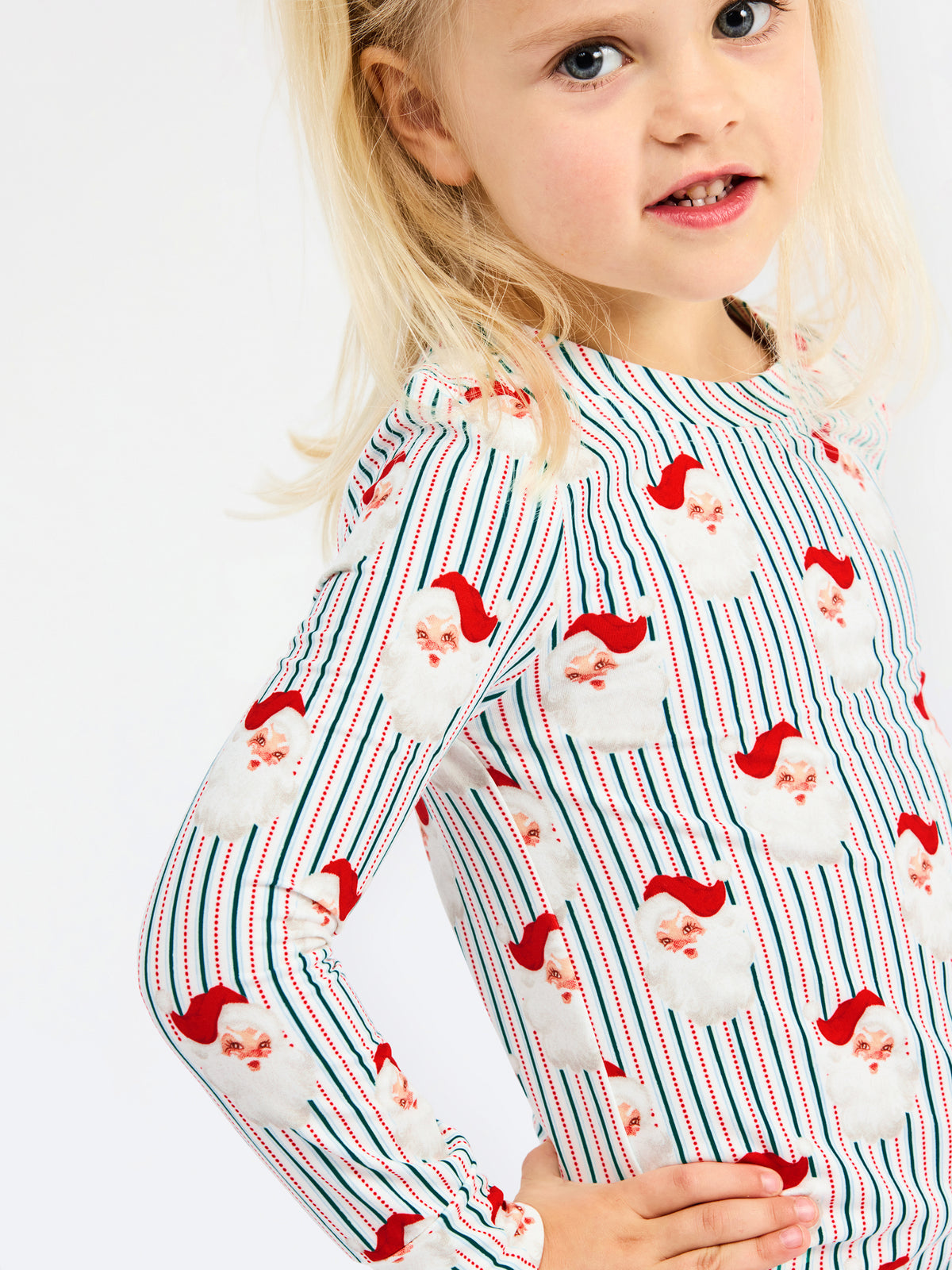 A young girl wearing a long-sleeve white top with red and blue vertical stripes and a Santa Claus face pattern, photographed against a plain white background.
