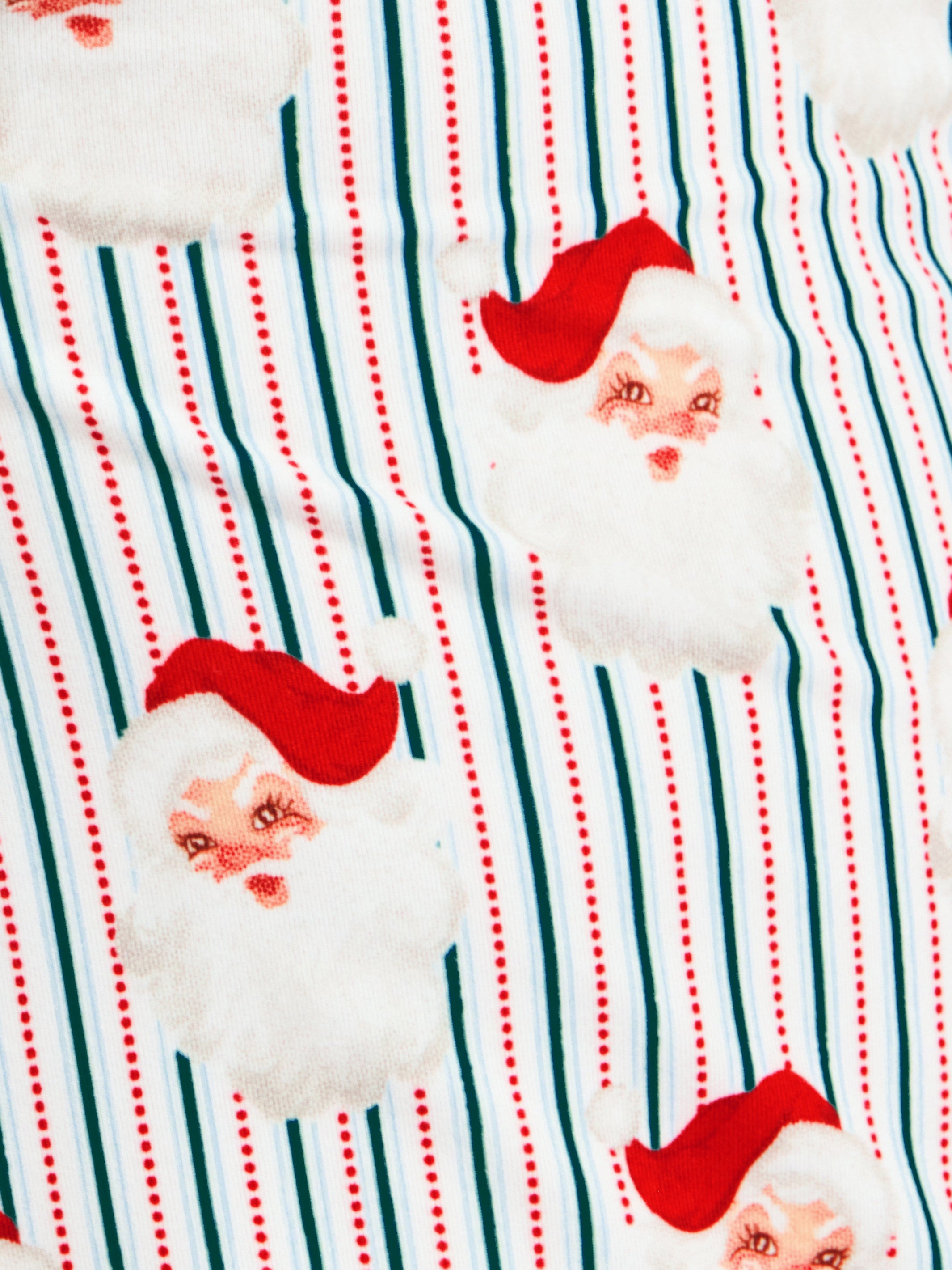 A close-up of a festive fabric print featuring Santa Claus faces with white fluffy beards and red hats, set against a background of green and red vertical stripes.