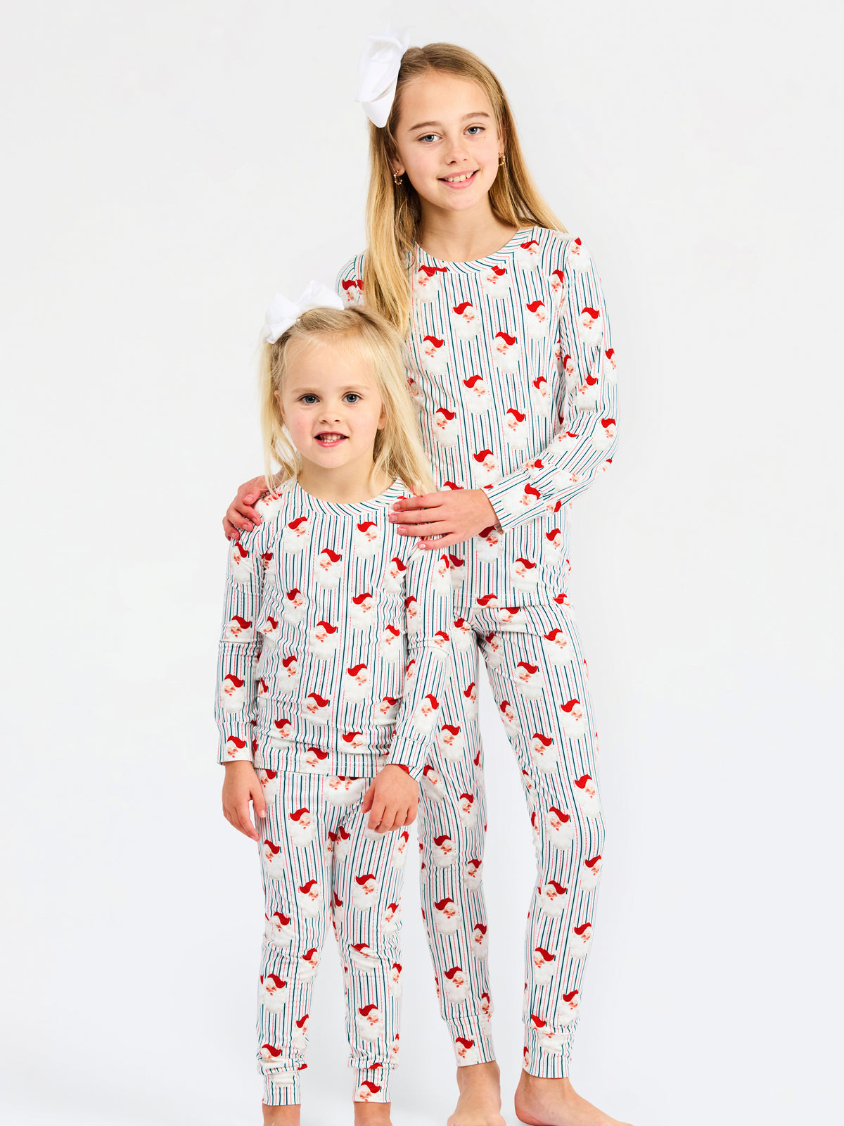 Two young girls modeling matching long-sleeve pajama sets with a white base, thin blue pinstripes, and a red bird print, posed against a plain white studio background.