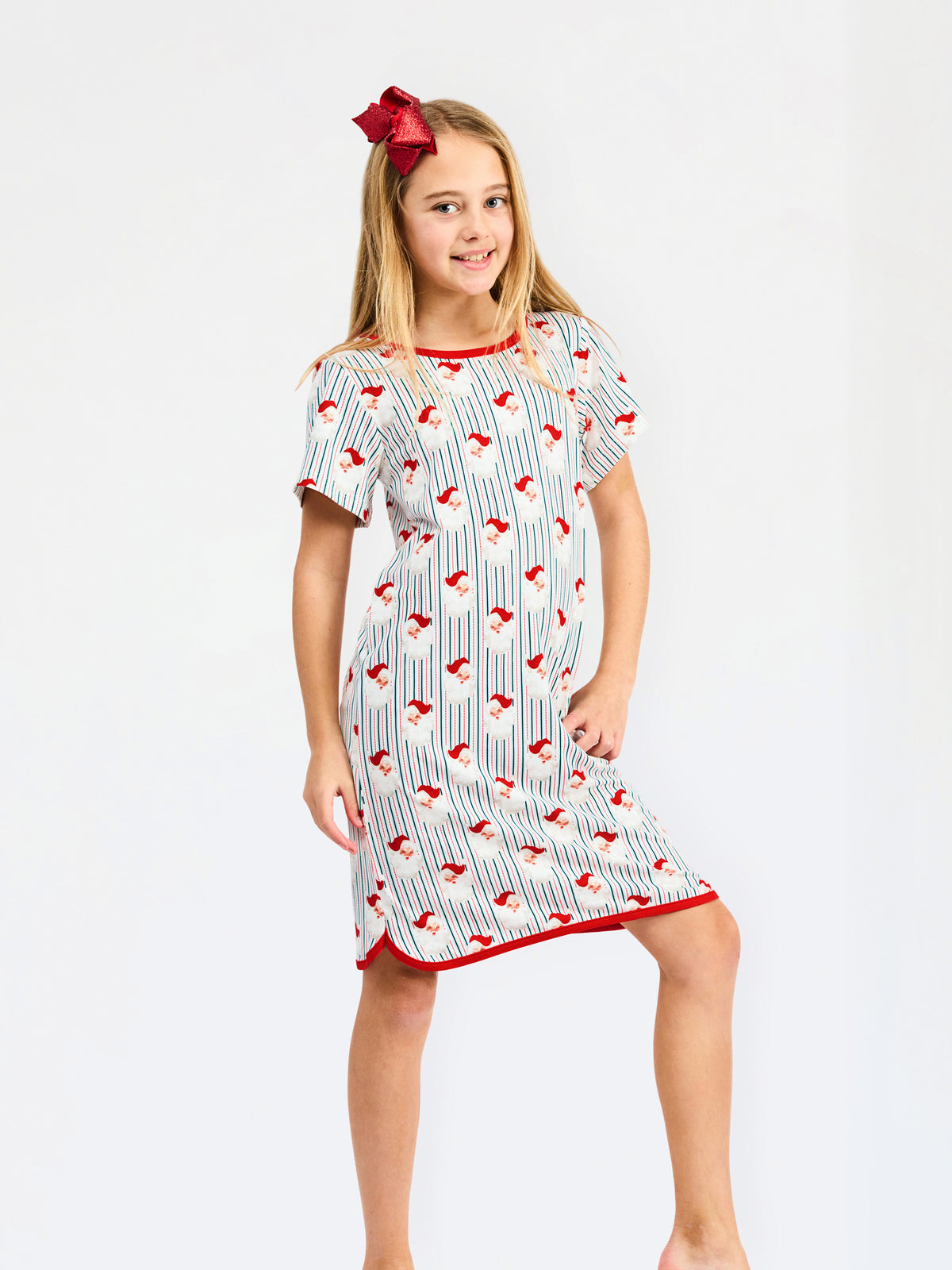 A young girl modeling a short-sleeve nightgown with a white base, red trim, and a repeating pattern of red birds on thin vertical blue stripes, set against a plain white studio background.