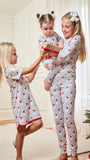Three children wearing matching holiday-themed pajamas with a red Santa Claus print on a white background, celebrating indoors near a Christmas tree.