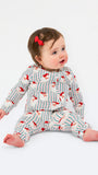 A baby sitting on a white studio background wearing a matching long-sleeve top and pants set with a red and blue striped pattern and small red bird motifs. The baby has a small red bow in their hair.