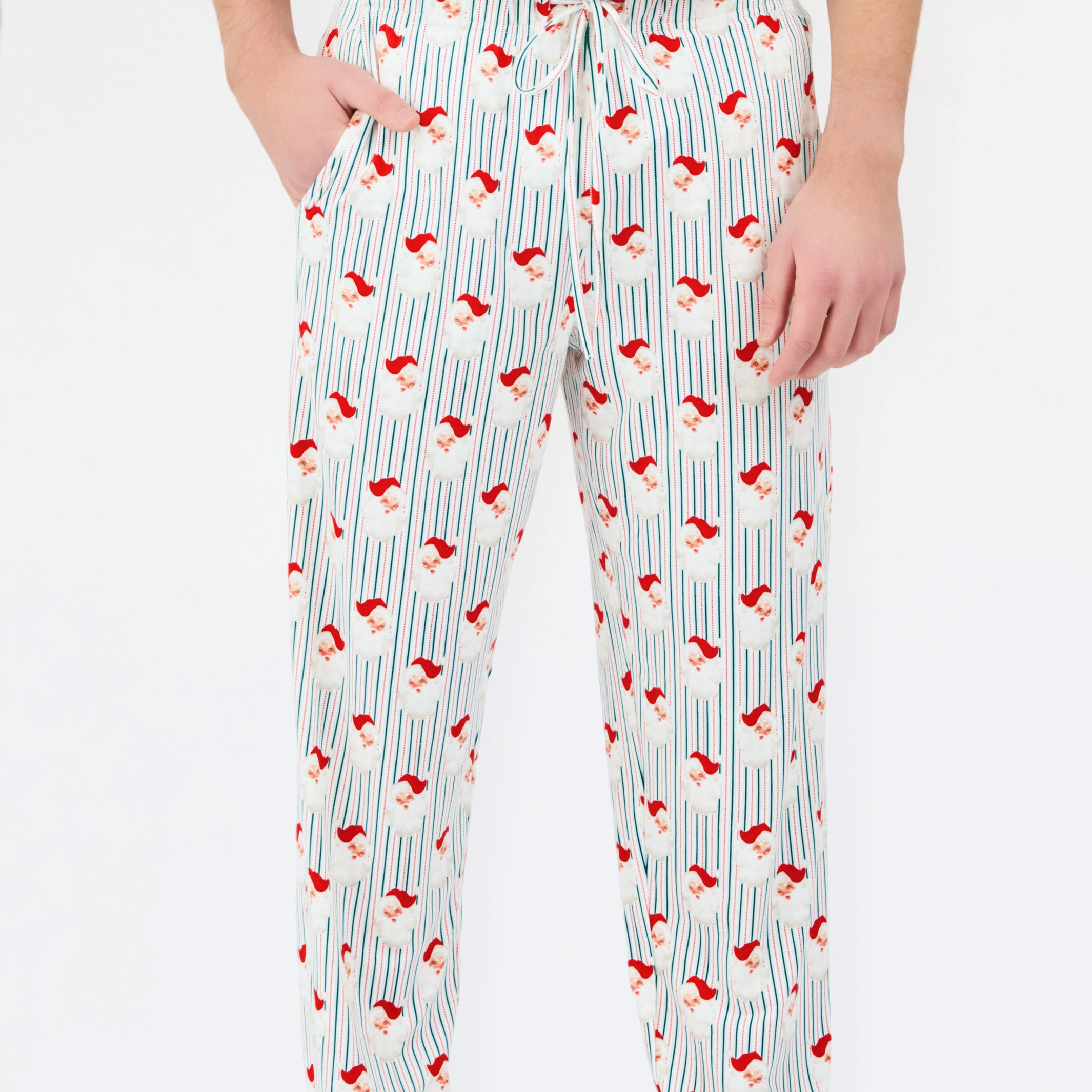 A person wearing white drawstring pants with a vertical blue stripe pattern and small red Santa hats printed throughout, paired with a white top against a plain white background.