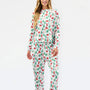 A woman modeling a matching long-sleeve top and pants pajama set with a festive Christmas print of Santa Claus, sleighs, and green trees on a white background.