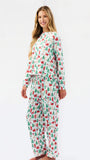 A woman modeling a matching long-sleeve pajama set with a festive Christmas print of Santa Claus, sleighs, and green trees on a white background, photographed against a seamless white studio backdrop.