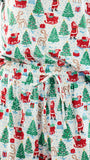 A close-up of a Christmas-themed fabric garment, likely a robe or dress, featuring a festive print of Santa Claus, reindeer, sleighs, and evergreen trees on a light blue background.
