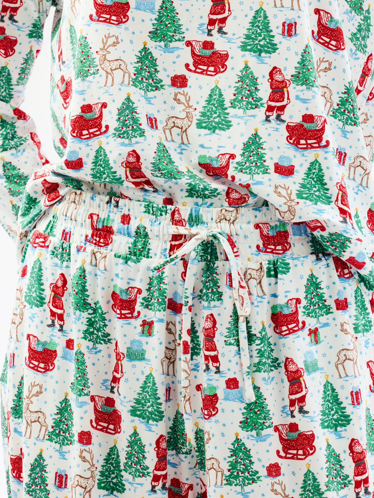 A close-up of a Christmas-themed fabric garment, likely a robe or dress, featuring a festive print of Santa Claus, reindeer, sleighs, and evergreen trees on a light blue background.