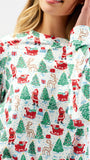 A close-up of a woman wearing a long-sleeve crewneck top with a festive Christmas print featuring Santa Claus, reindeer, sledding, and Christmas trees on a white background.