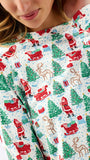 A close-up of a person wearing a white long-sleeve top with a festive Christmas print featuring Santa Claus, reindeer, sledding, and evergreen trees.