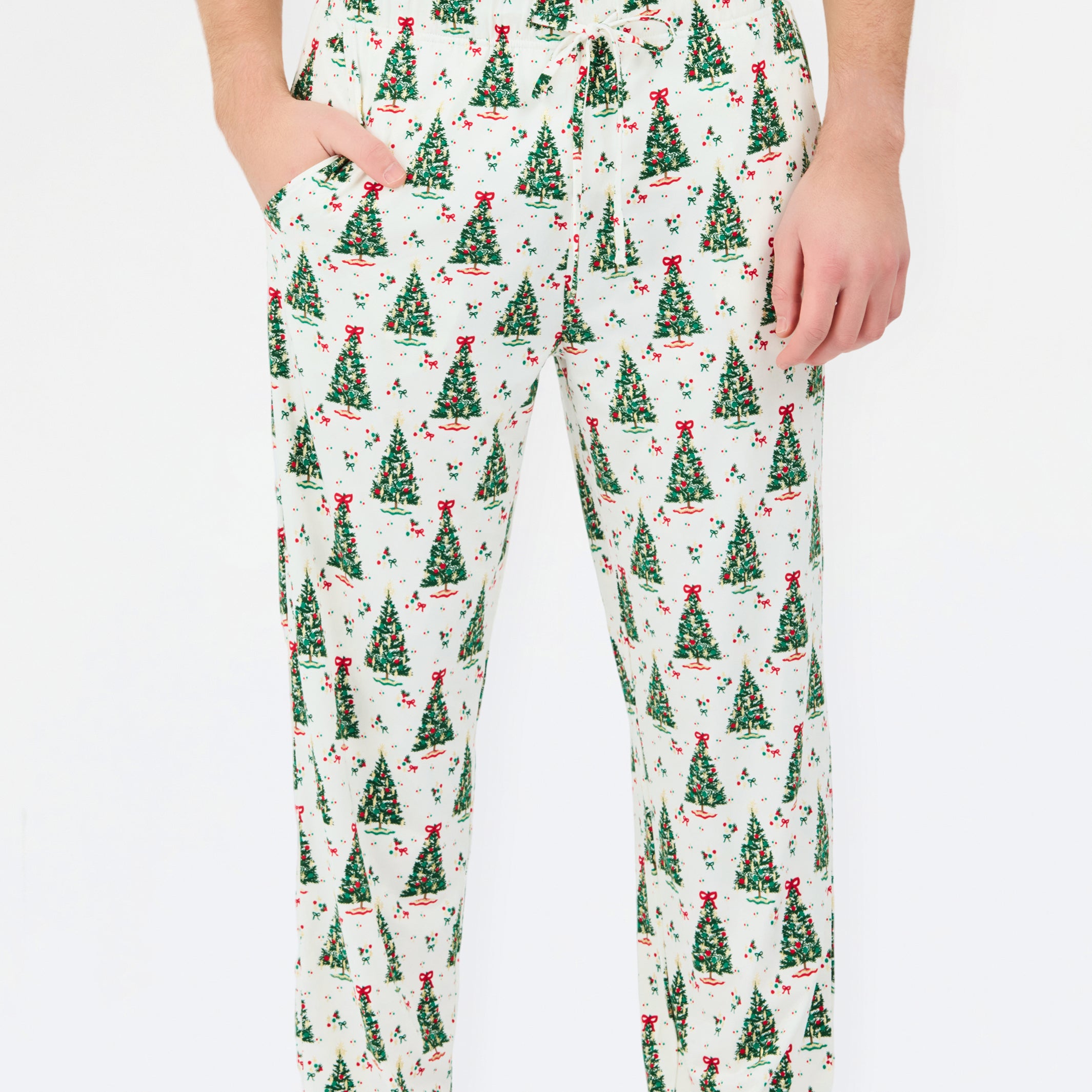 A person wearing white drawstring pants with an all-over green Christmas tree print, paired with a white top and white socks, against a plain white background.