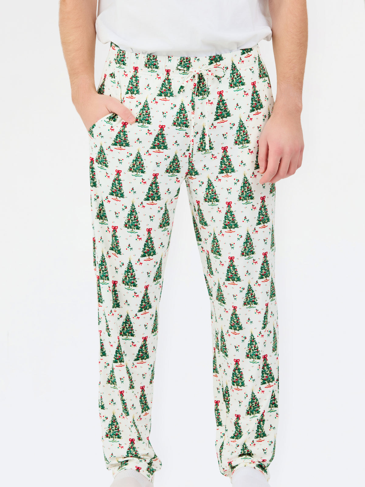 A person wearing white drawstring pants with an all-over green Christmas tree print, paired with a white top and white socks, against a plain white background.