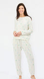 A woman modeling a two-piece pajama set consisting of a long-sleeve top and matching pants, both in an off-white color with a small, scattered pine tree pattern in light green, blue, and pink.