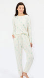 A woman modeling a two-piece long-sleeve pajama set with a white base and a small repeating pattern of green, blue, and pink pine trees, photographed against a plain white studio background.