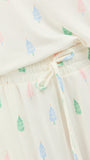 Close-up of a cream-colored pajama set with a repeating pattern of small pine trees in green, blue, and pink, featuring an elastic waistband and drawstring.