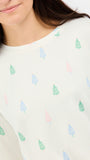A close-up of a person wearing a cream-colored long-sleeve top with a repeating pattern of small pine trees in pastel green, blue, and pink.