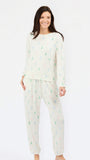 A woman modeling a two-piece pajama set featuring a cream-colored long-sleeve top and matching pants, both decorated with a small, repeating multicolor pine tree pattern in green, blue, and pink.