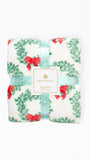 A folded Mary Square floral blanket with a green wreath and red bow pattern, wrapped in a light blue ribbon with a white brand label.