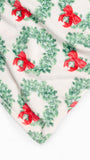 A close-up of a soft textile with a repeating holiday wreath and red bow print on an off-white background.