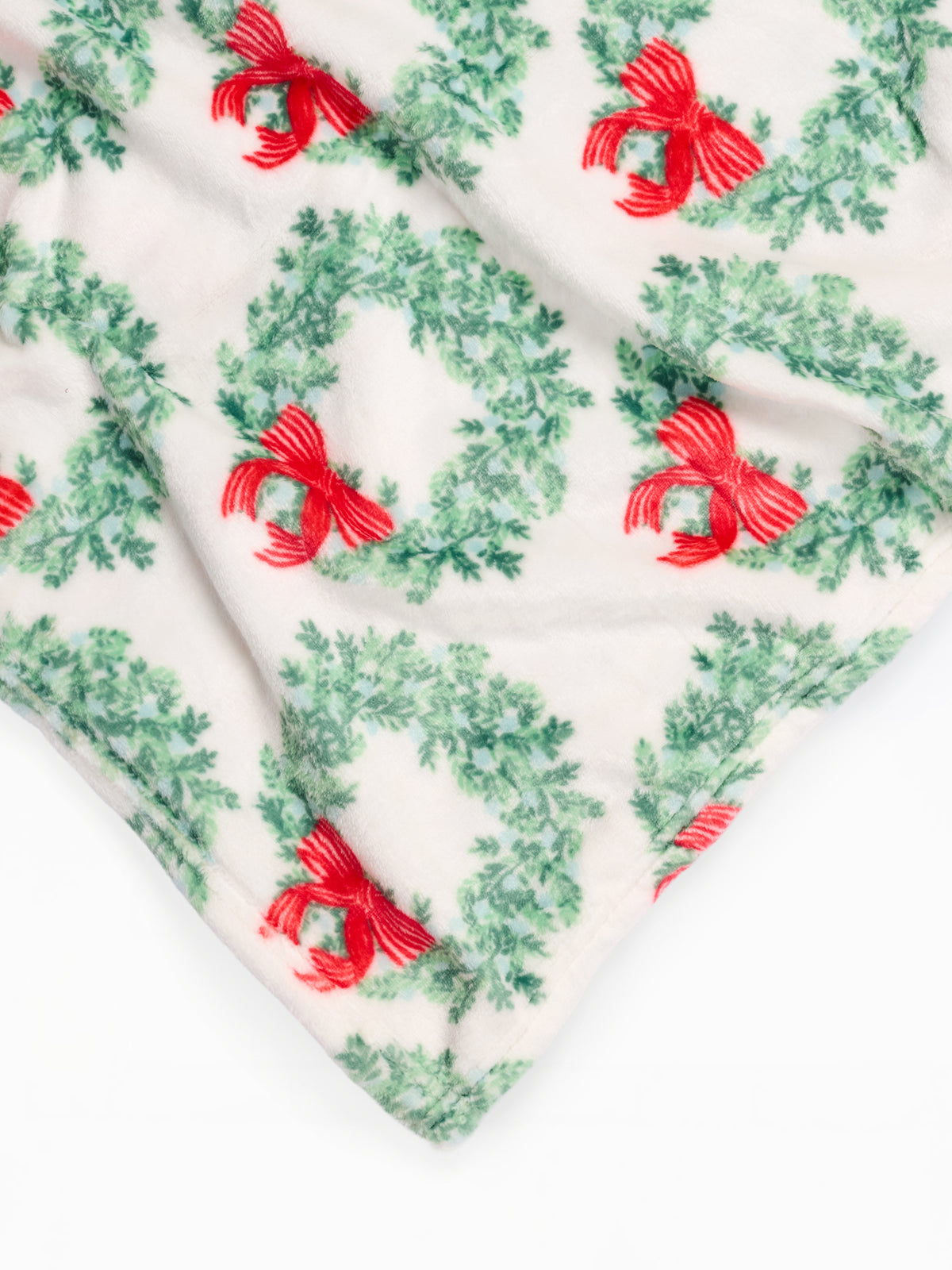 A close-up of a soft textile with a repeating holiday wreath and red bow print on an off-white background.