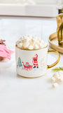 A white ceramic mug with a gold handle and rim, decorated with a festive Christmas scene featuring Santa Claus, a reindeer, and a tree. The mug is filled with white marshmallows and styled on a light tabletop with holiday props.