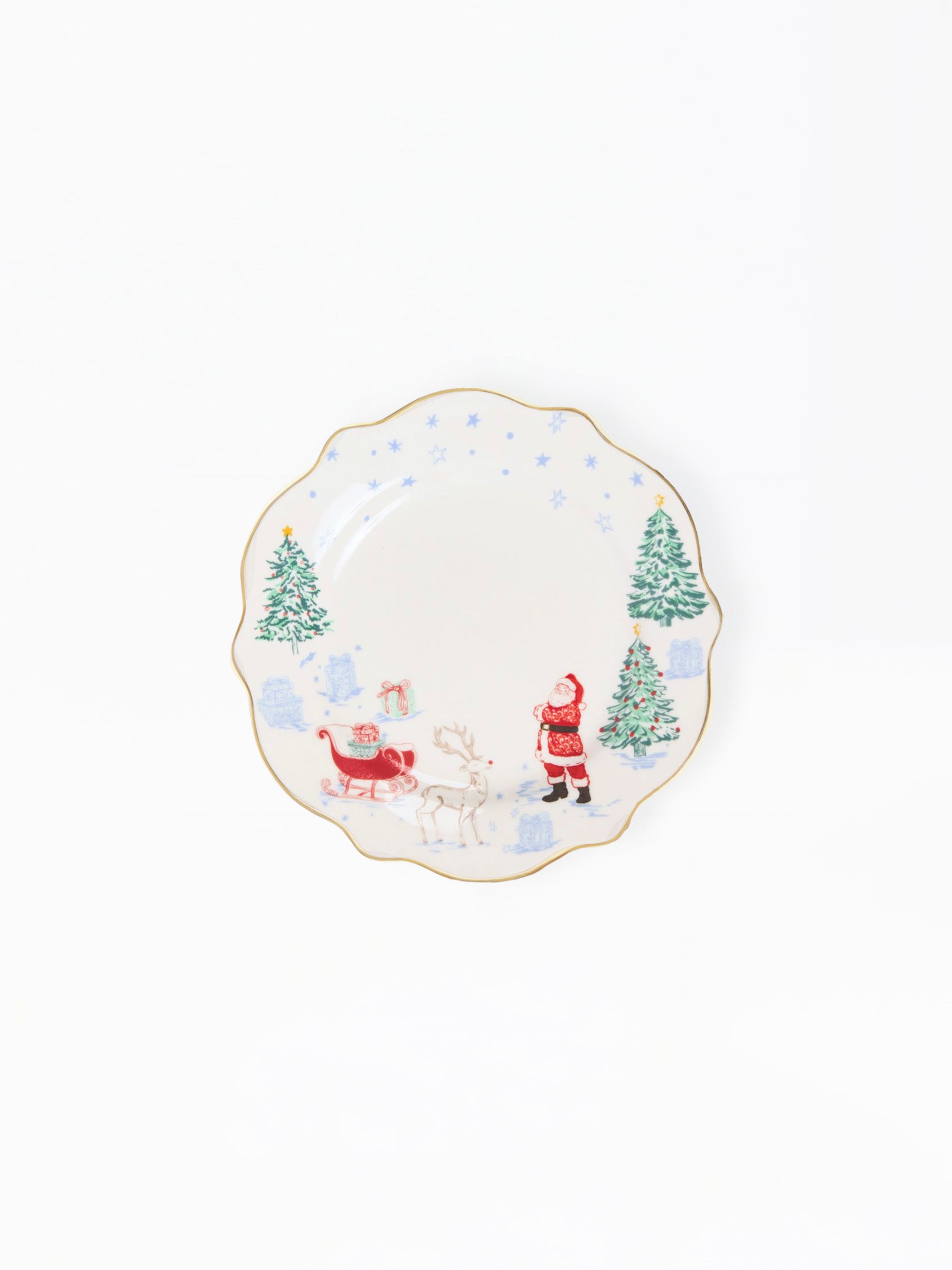A scalloped ceramic plate with a festive Christmas design, featuring Santa Claus, a reindeer, and snow-covered pine trees on a white background with a thin gold rim.