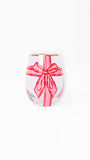 A clear stemless wine glass featuring a pink gift box design with a red ribbon and bow, finished with a gold rim, set against a plain white background.