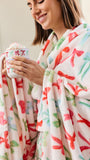 A woman wrapped in a soft fleece blanket with a colorful dragonfly pattern, holding a mug topped with whipped cream and hot chocolate.