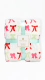 A folded Mary Square fleece blanket with a white background and a repeating bow pattern in red, pink, and light green, wrapped in a mint green ribbon with a central brand label.