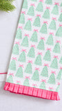A close-up of a white fabric item, likely a towel or napkin, featuring a repeating pattern of green Christmas trees with pink bows and a pink pleated ruffle trim along the bottom edge.