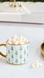 A white ceramic mug with a gold handle and rim, decorated with a green Christmas tree and blue damask pattern, filled with mini marshmallows on a white countertop.